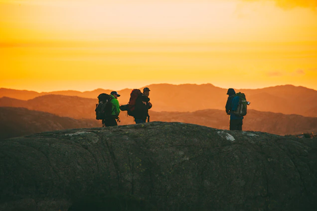 A minimalist dark-themed photo of hikers silhouetted against a forest green mountain backdrop at dusk.