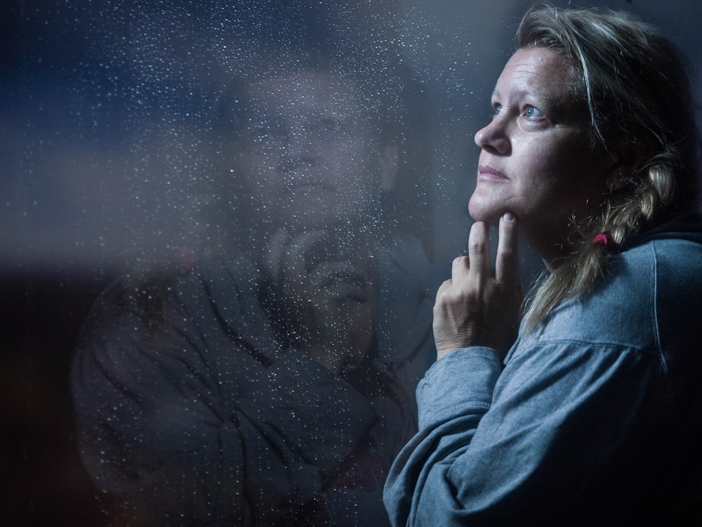 clear glass window panel casting reflection of woman touching her jaw