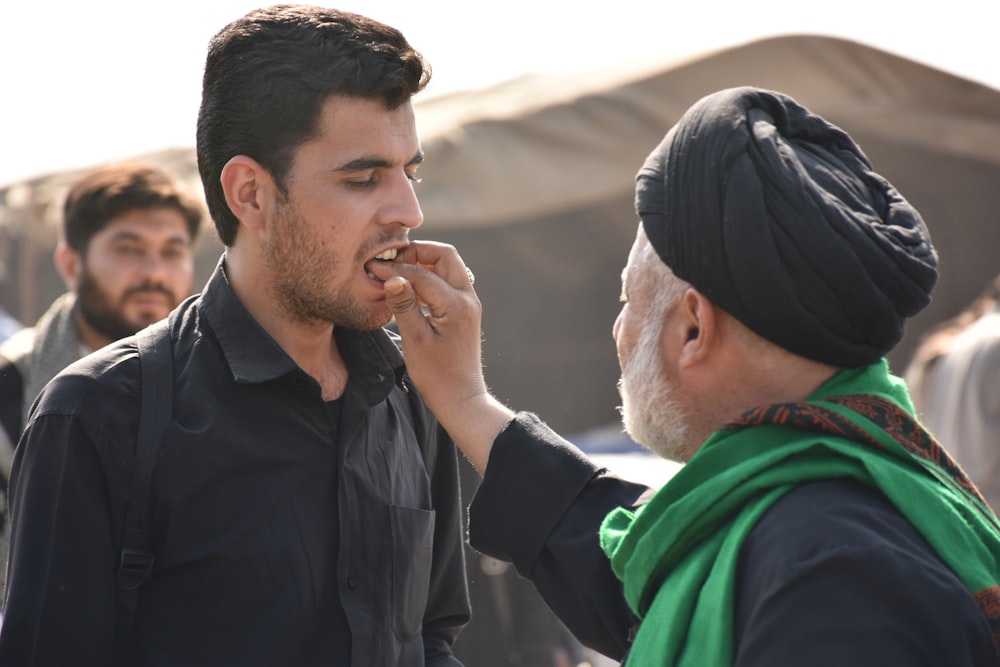 man wearing green scarf touching the mouth of man in black dress shirt