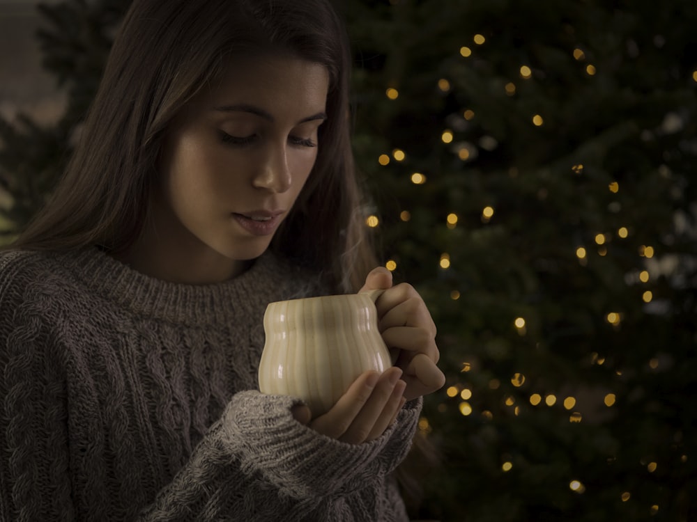 man holding white ceramic mug standing in front of lighted green Christmas tree