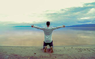 man wearing gray long-sleeved shirt beside seashore during daytime