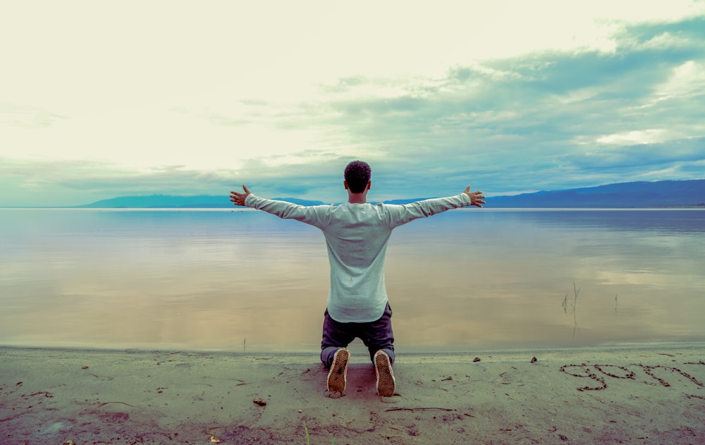 man wearing gray long-sleeved shirt beside seashore during daytime