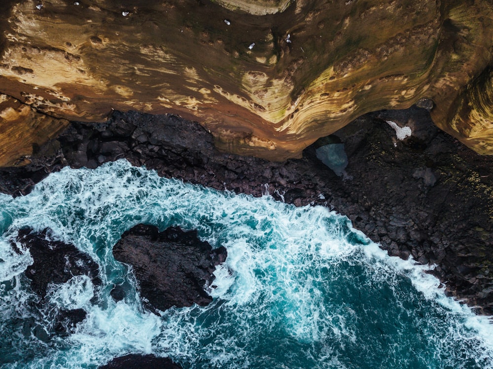 top-view photography of waves crashing on black rocks at daytime