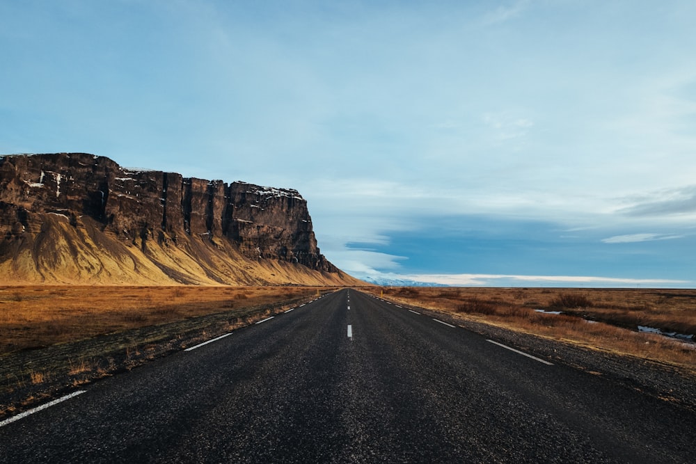 gray asphalt road in the middle of desert near black mountain during daytime