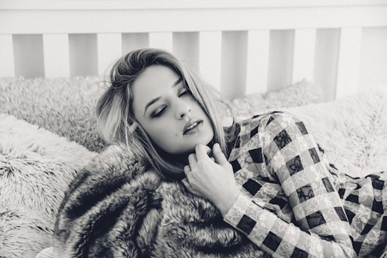 A cozy bedroom scene featuring a woman wearing a silk pajama set, surrounded by silk pillowcases and a sleep mask.