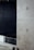 A minimalist interior space featuring a large concrete wall with visible construction markings and a metal railing in the foreground. The background is dark, adding contrast to the lighter tones of the concrete. The overall design is industrial and modern.