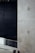 A minimalist interior space featuring a large concrete wall with visible construction markings and a metal railing in the foreground. The background is dark, adding contrast to the lighter tones of the concrete. The overall design is industrial and modern.