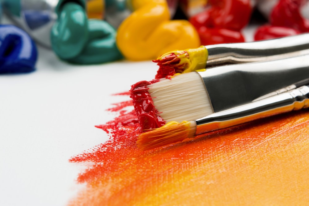 three silver paint brushes on white textile