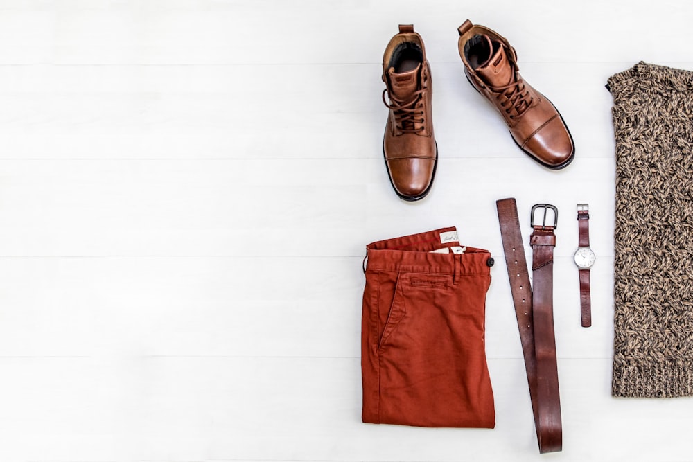 par de botas de couro marrom, shorts vermelhos, cinto de couro marrom, relógio redondo dourado e top marrom
