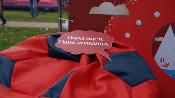 A speech bubble with text in the Russian language is placed over a red and black bean bag. The background features a red display with white cloud and circle graphics.