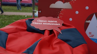 A speech bubble with text in the Russian language is placed over a red and black bean bag. The background features a red display with white cloud and circle graphics.