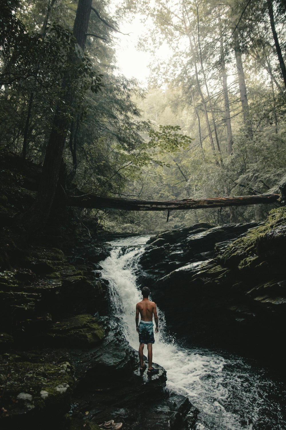 man wearing teal and black shorts standing beside waterfalls