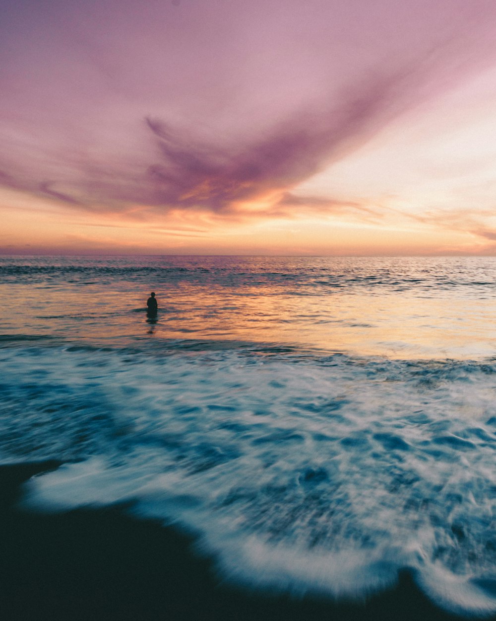 person standing on blue ocean water during orange sunset