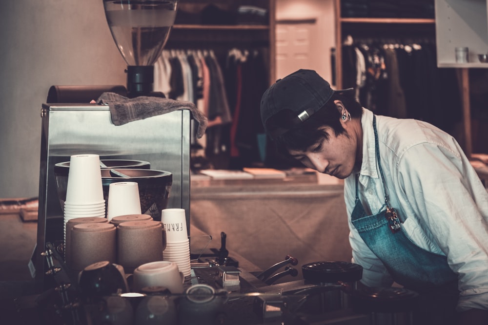 man facing kitchenware and appliances wearing white top and blue apron