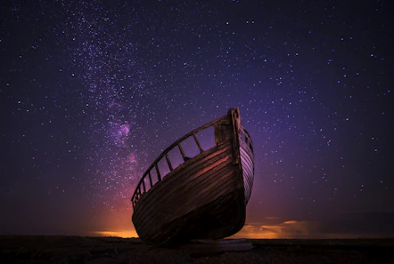 An old wooden boat hull silhouetted against a vibrant purple starry night sky