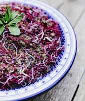 Sunlit shot of green lentils scattered across a wooden table with fresh herbs.