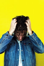 man in blue denim jacket holding his hair