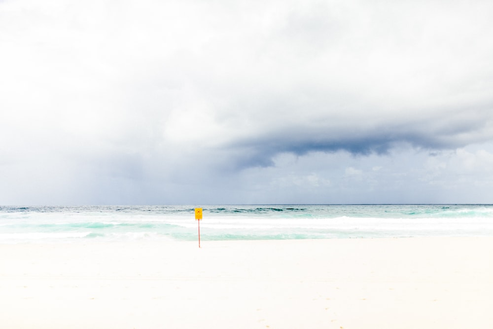 yellow pole on seashore under white clouds