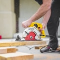 man in black sweatpants using DEWALT circular saw and cutting a wood plank