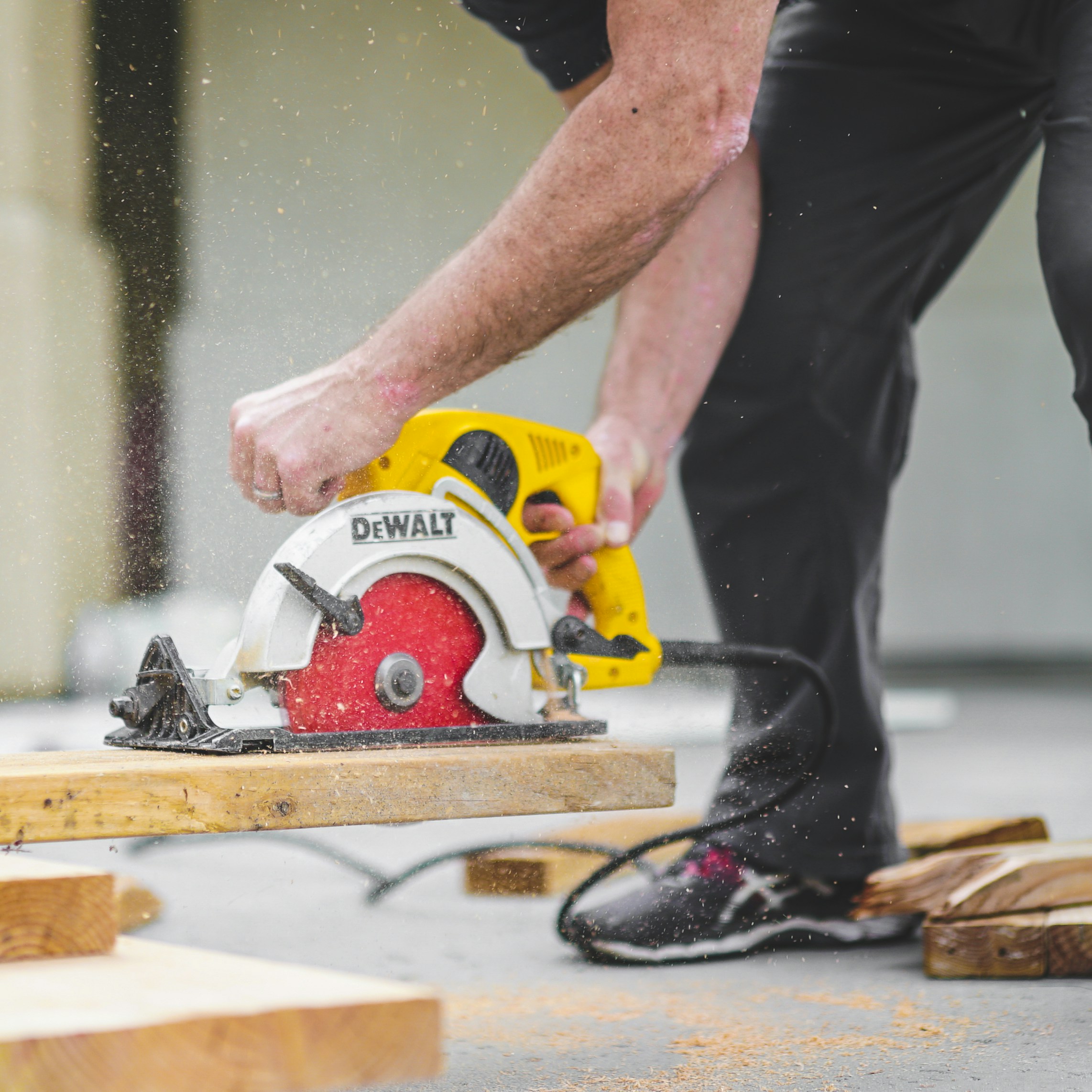 man in black sweatpants using DEWALT circular saw and cutting a wood plank