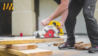 man in black sweatpants using DEWALT circular saw and cutting a wood plank