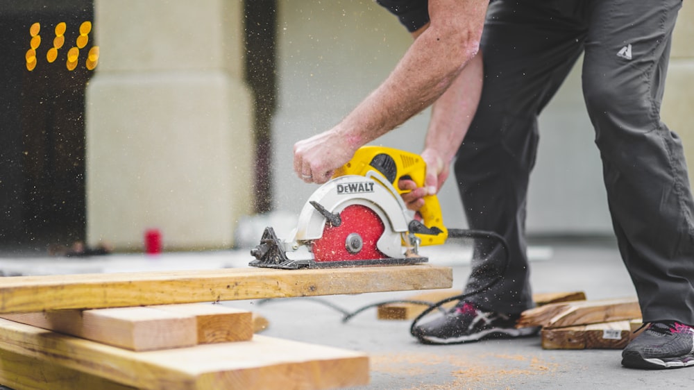 hombre con pantalones de chándal negros usando una sierra circular DEWALT y cortando un tablón de madera