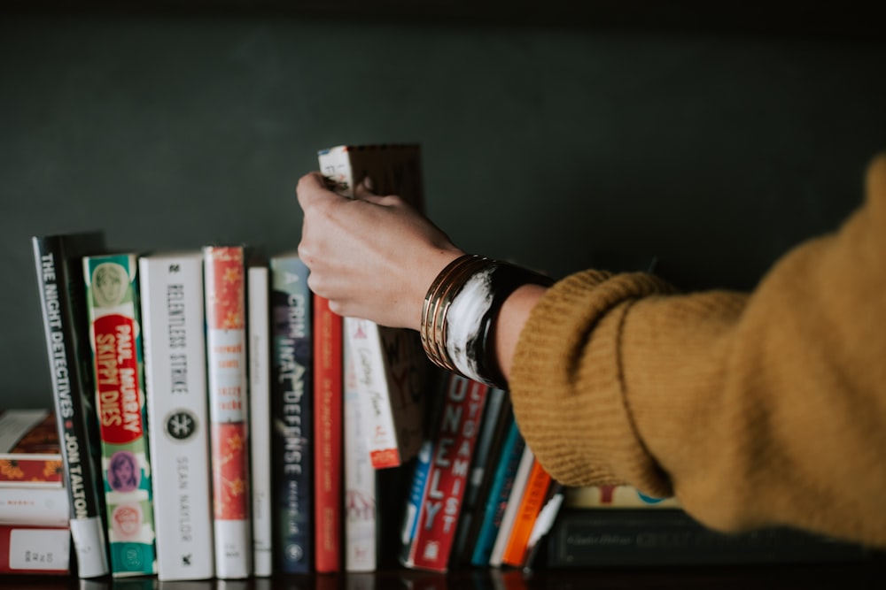 person picking white and red book on bookshelf