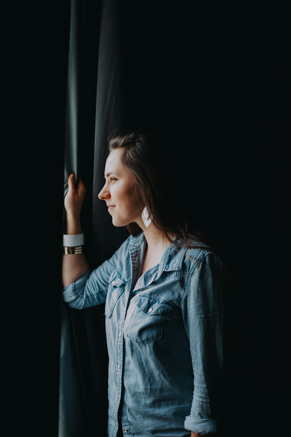 woman wearing chambray button-up top looking through the window