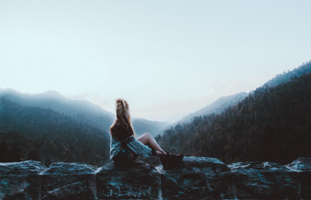 Frau sitzt auf grauem Felsen mit Blick auf grüne Berge
