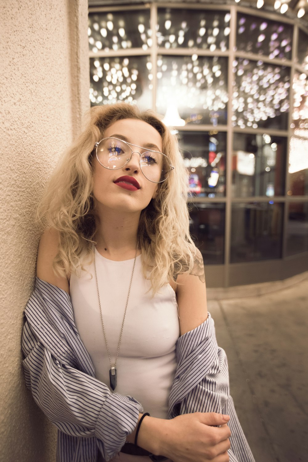 woman leaning on white painted concrete wall wearing white sleeveless top with white and black striped long-sleeved shirt