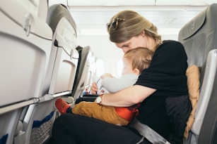 woman carrying baby while sitting on grey seat on plane