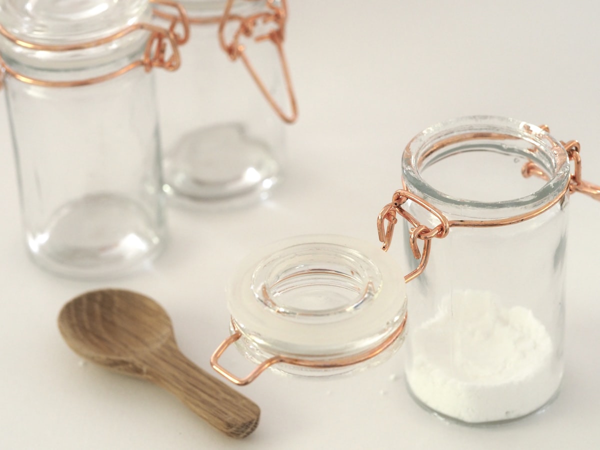 Frascos de vidrio con cierre hermético llenos de polvo blanco de bicarbonato de sodio junto a una cuchara de madera sobre fondo claro