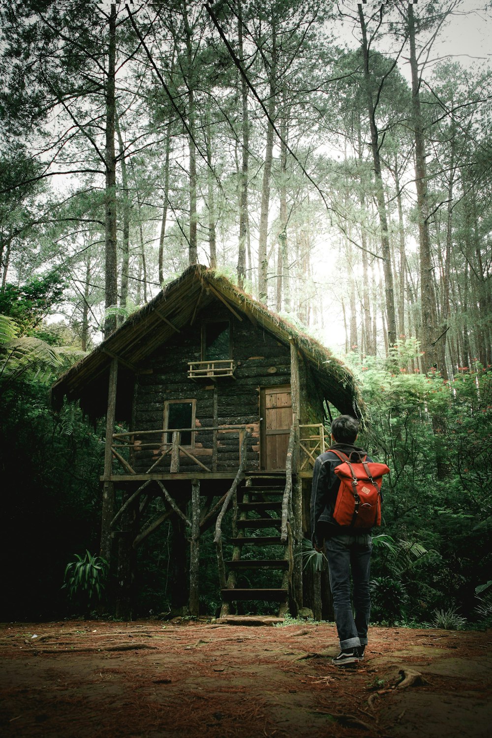 homem com mochila ao lado de uma casa de madeira na floresta
