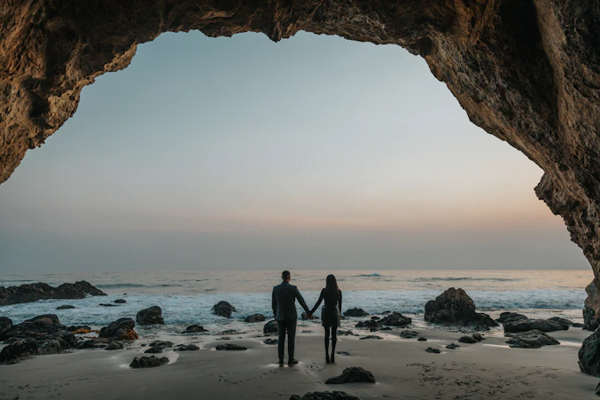 man and woman holding hands facing sea