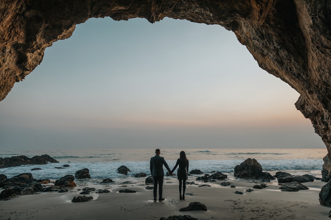 man and woman holding hands facing sea,