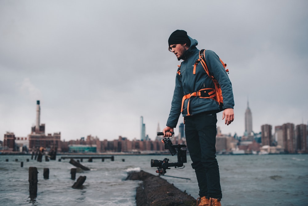 man wearing teal zip-up bubble jacket taking photo of body of water with camera with stabilizer