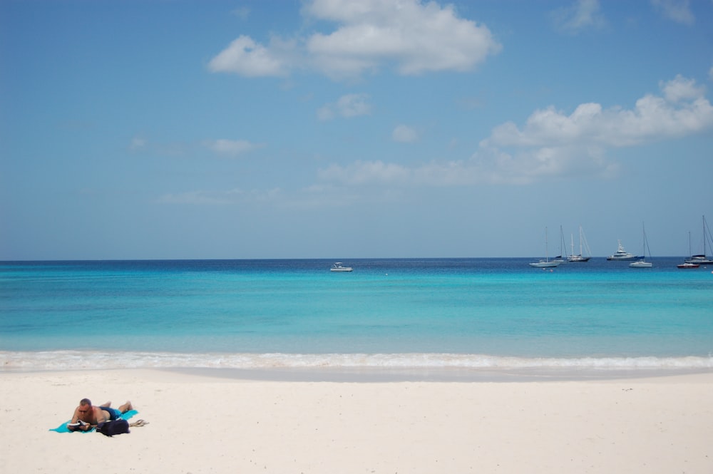 man laying on beach in distant of boats