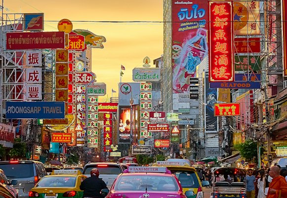 Vehicles on street between buildings with Kanji script signage during golden hour — Bangkok, Thailand
