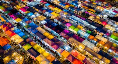 An aerial view of a bustling travel market with colorful stalls and lively crowds.