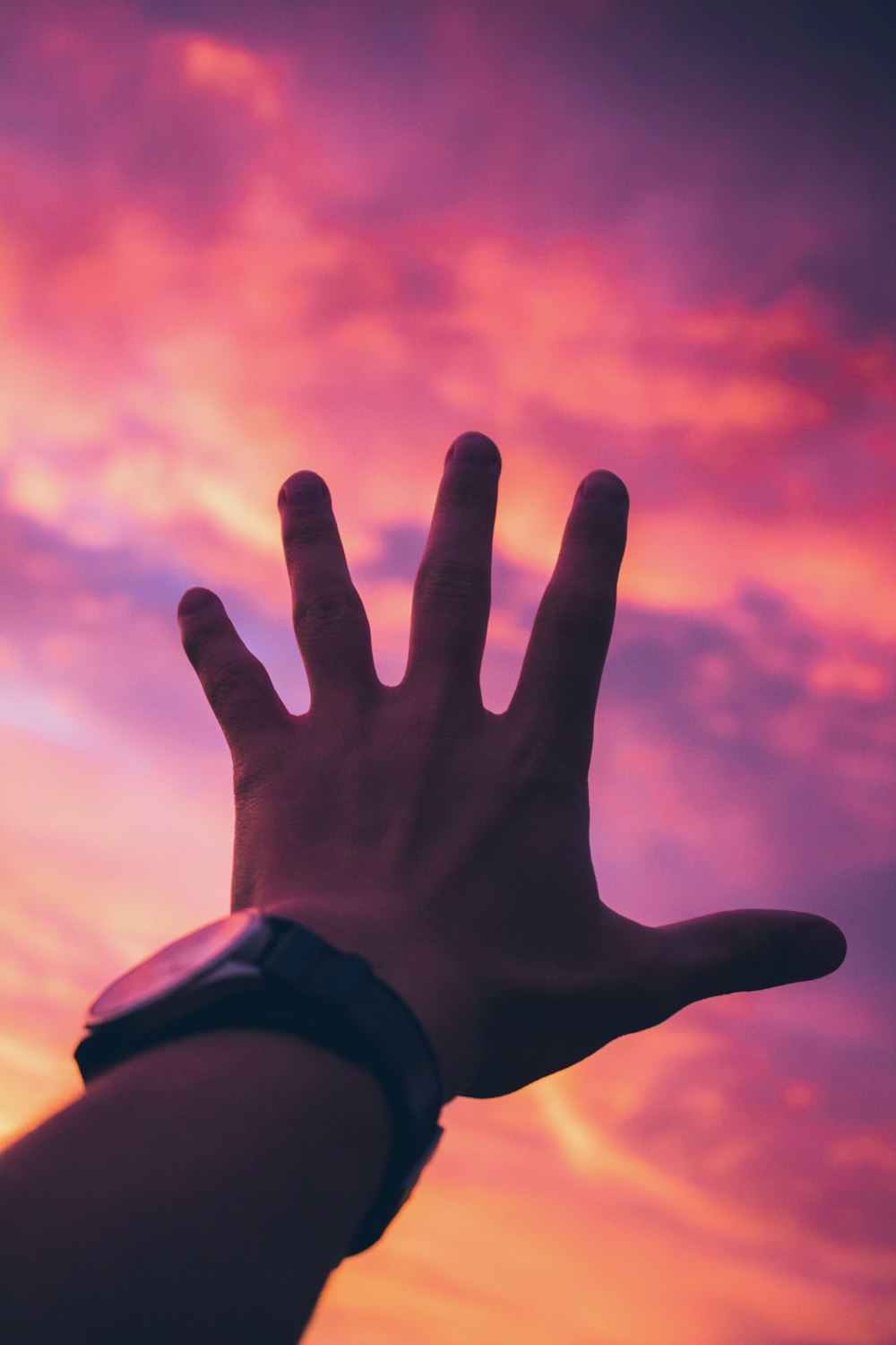 person with black watch reaching for orange sky