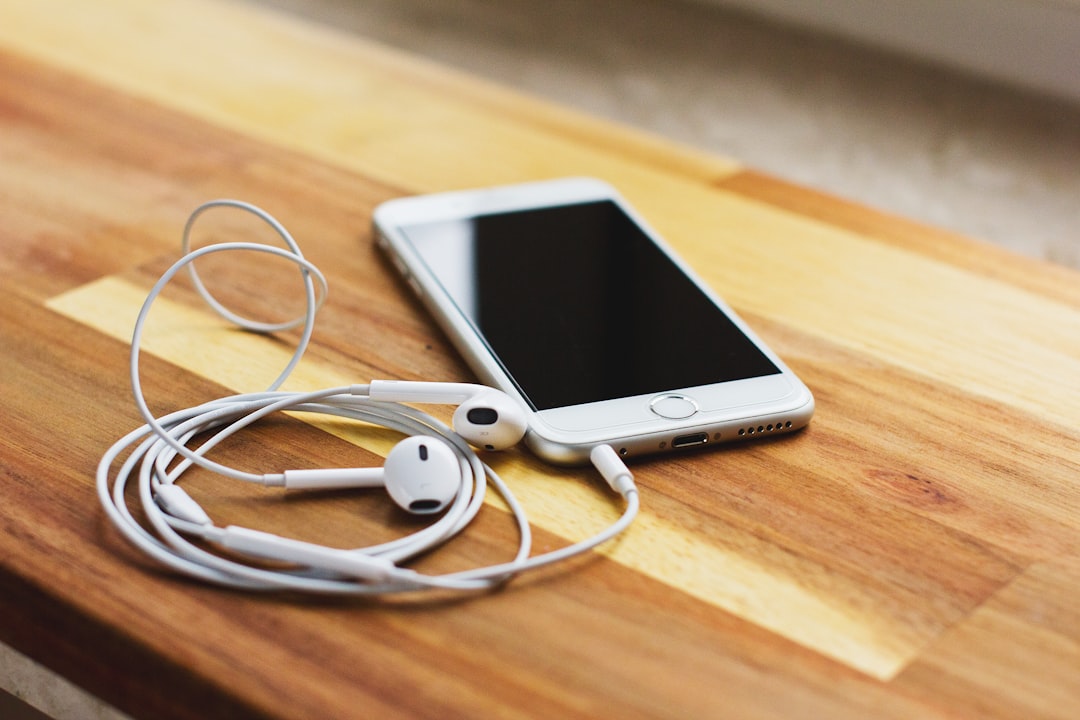 silver iPhone 6 with EarPods on brown wooden table,