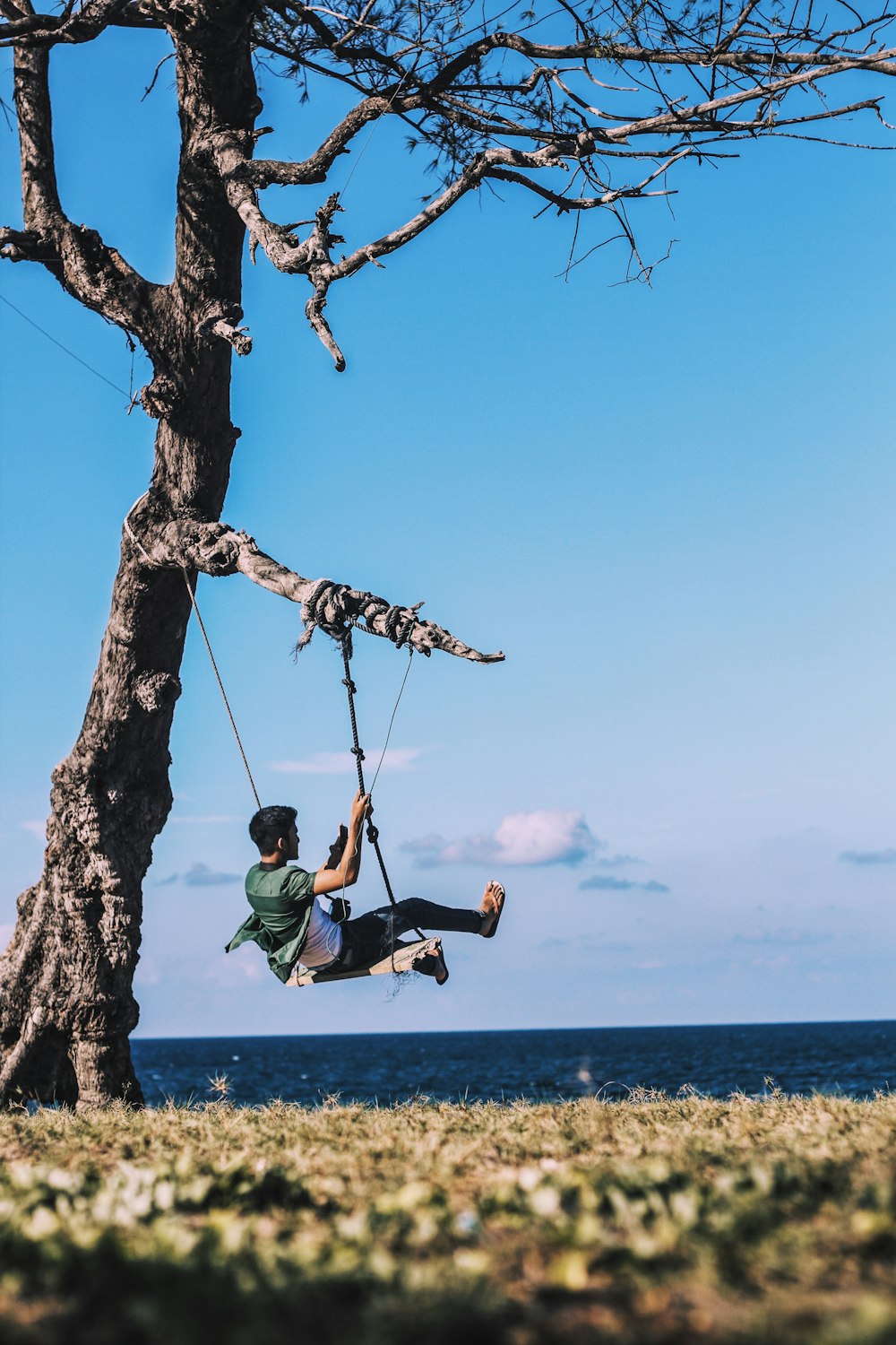 man on swing mounted on tree near body of water