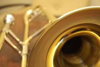 A close-up view of a brass trombone, emphasizing its shiny golden bell. The instrument's metallic structure is highlighted with intricate reflections and details.