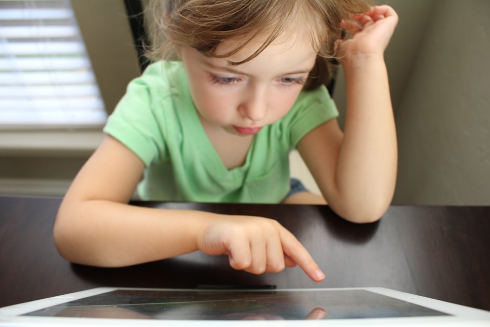 girl sitting beside the table while operating tablet computer