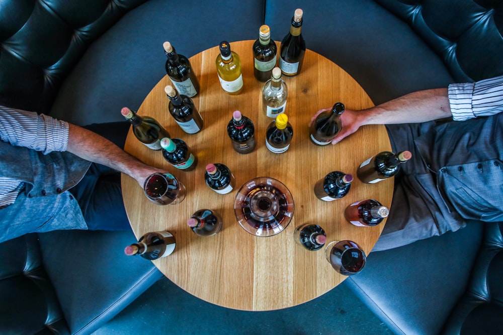 person holding glass bottle on round brown wooden table