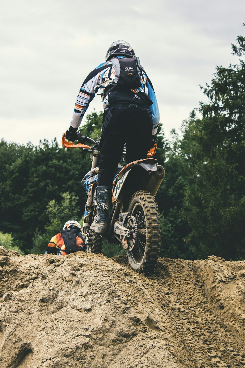 man riding motocross motorcycle over mound near trees during daytime