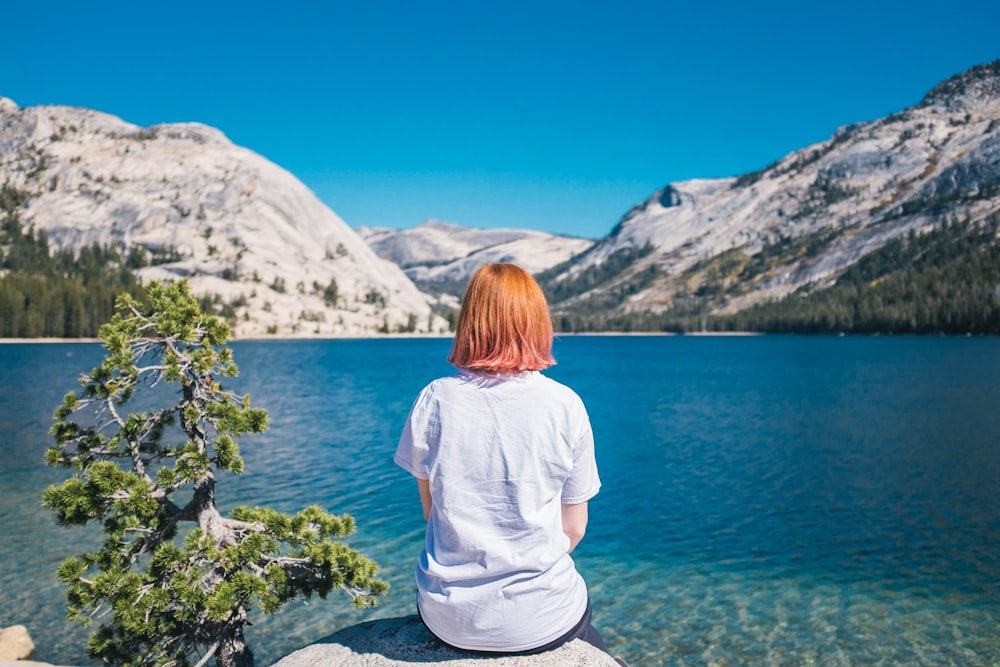 woman sitting on the stone facing the ocean and mountain