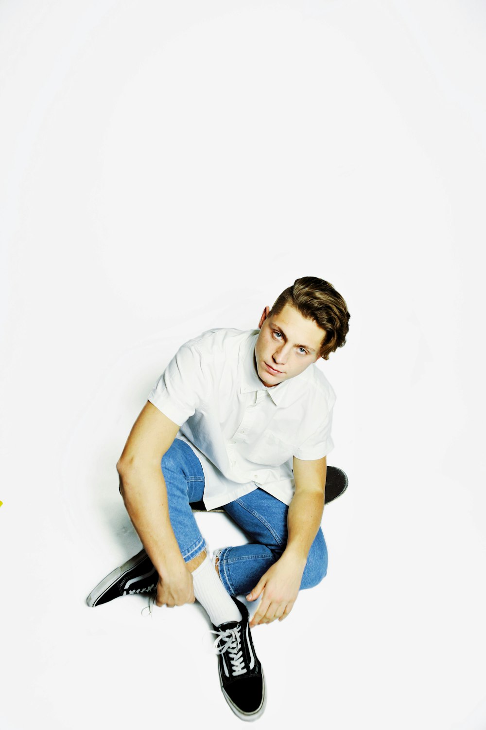 man wearing white dress shirt and blue denim jeans sitting on floor