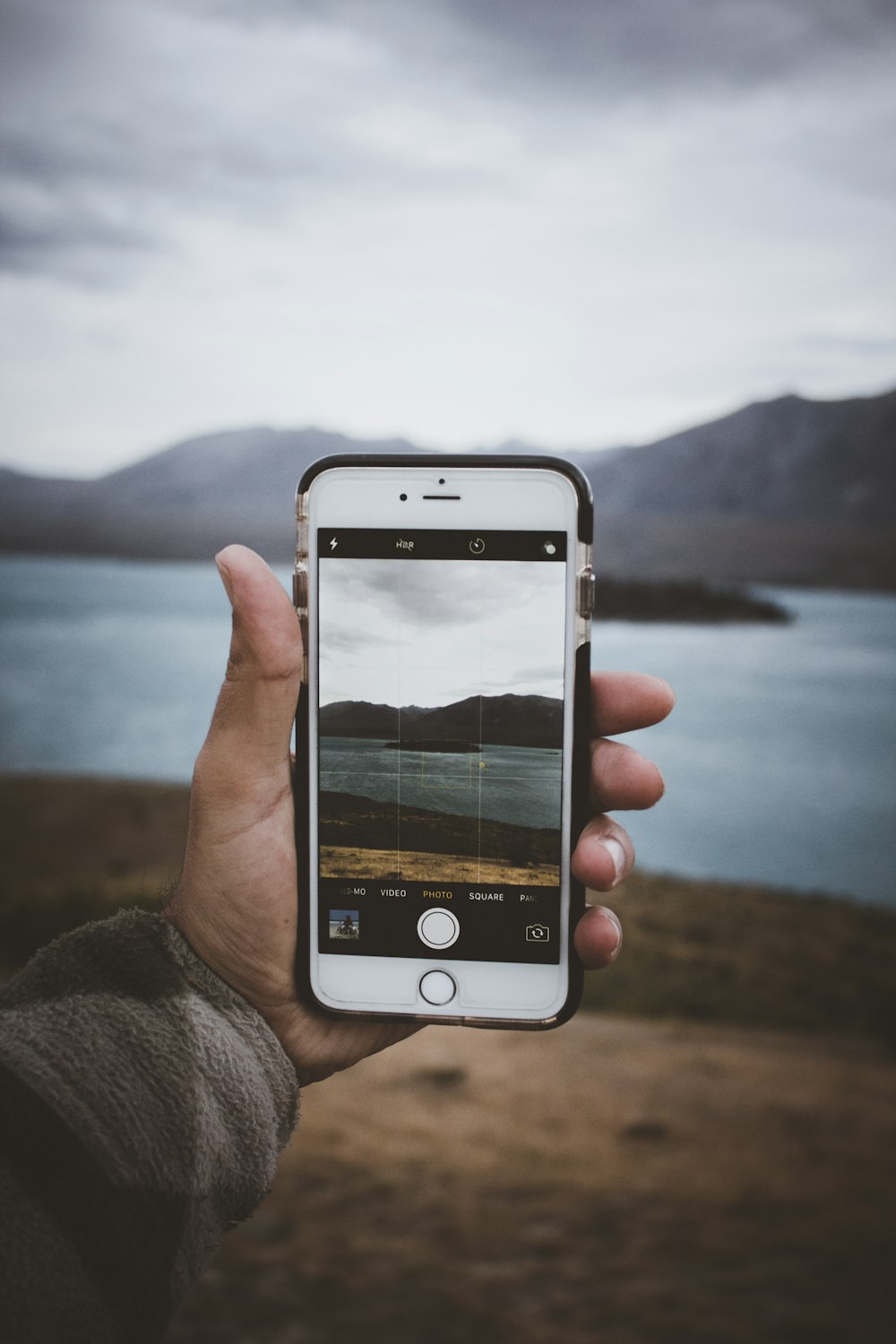 person holding gold iPhone 6 taking a photo of lake surrounded island during daytime