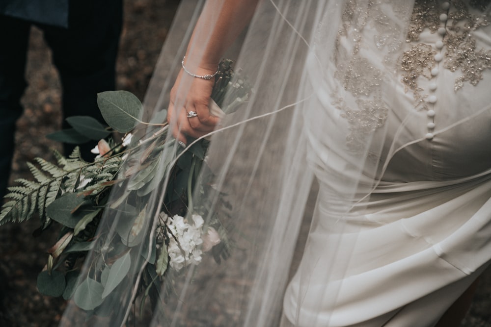 femme portant une robe de mariée blanche tenant un bouquet de fleurs